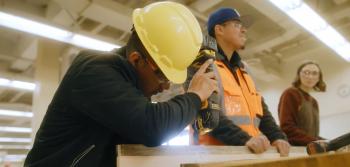 Student wearing hardhat working on wood beam