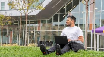 Student sitting on grass while working on laptop