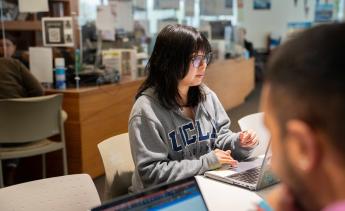 Student wearing UCLA sweatshirt working on laptop 