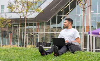 Student sitting on grass while working on laptop