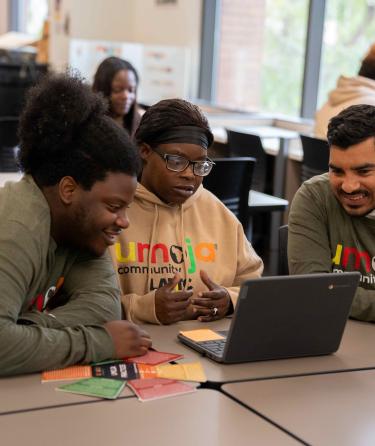 Three students wearing Umoja shirts looking at a laptop