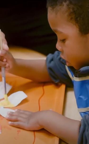 Child painting a flower with assistance of Child Development employee