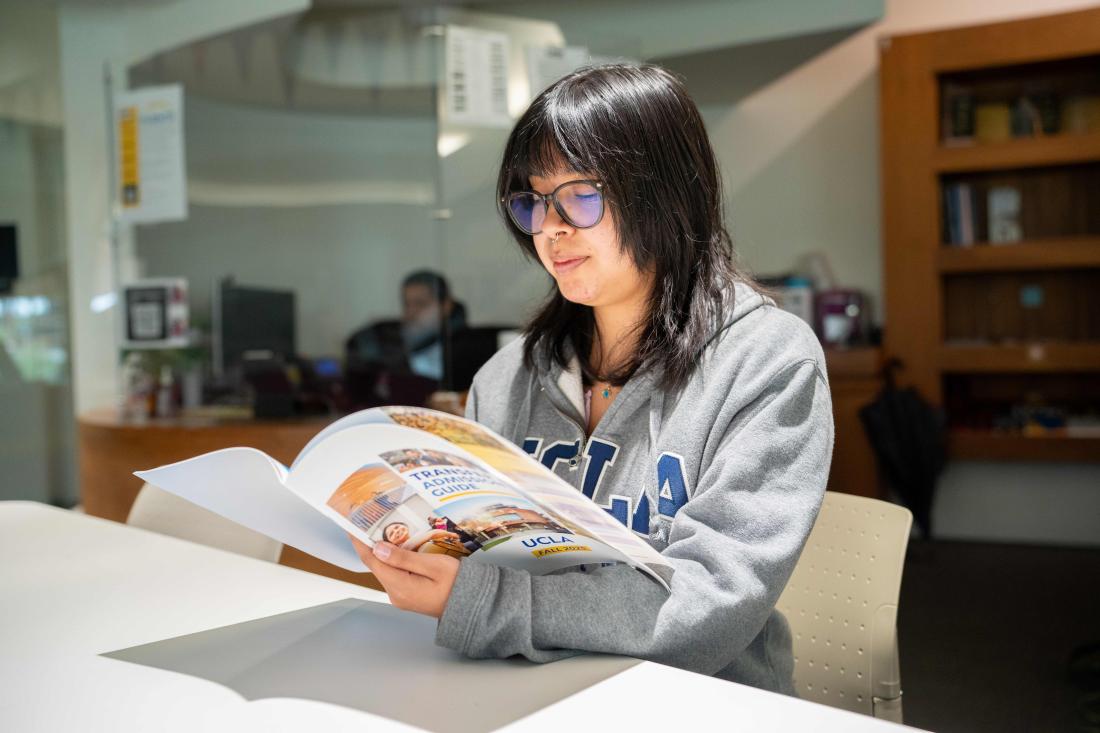 Student wearing a UCLA sweatshirt and browsing a transfer brochure