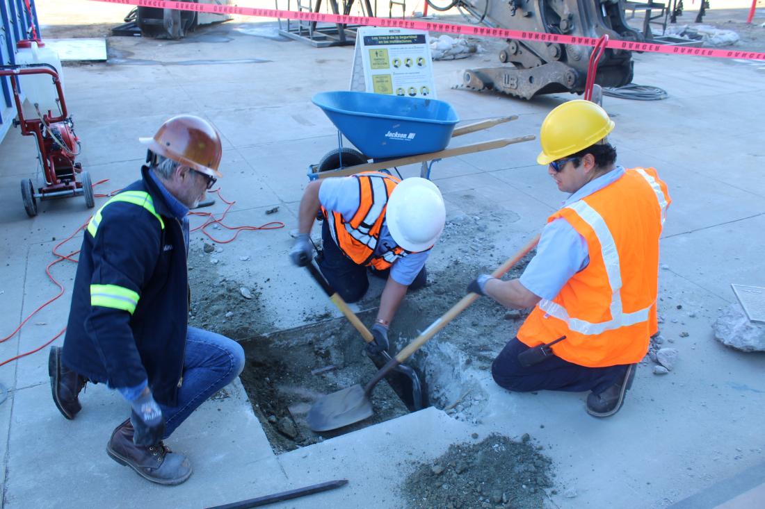Physical plant workers lifting time capsule out of ground with shovels