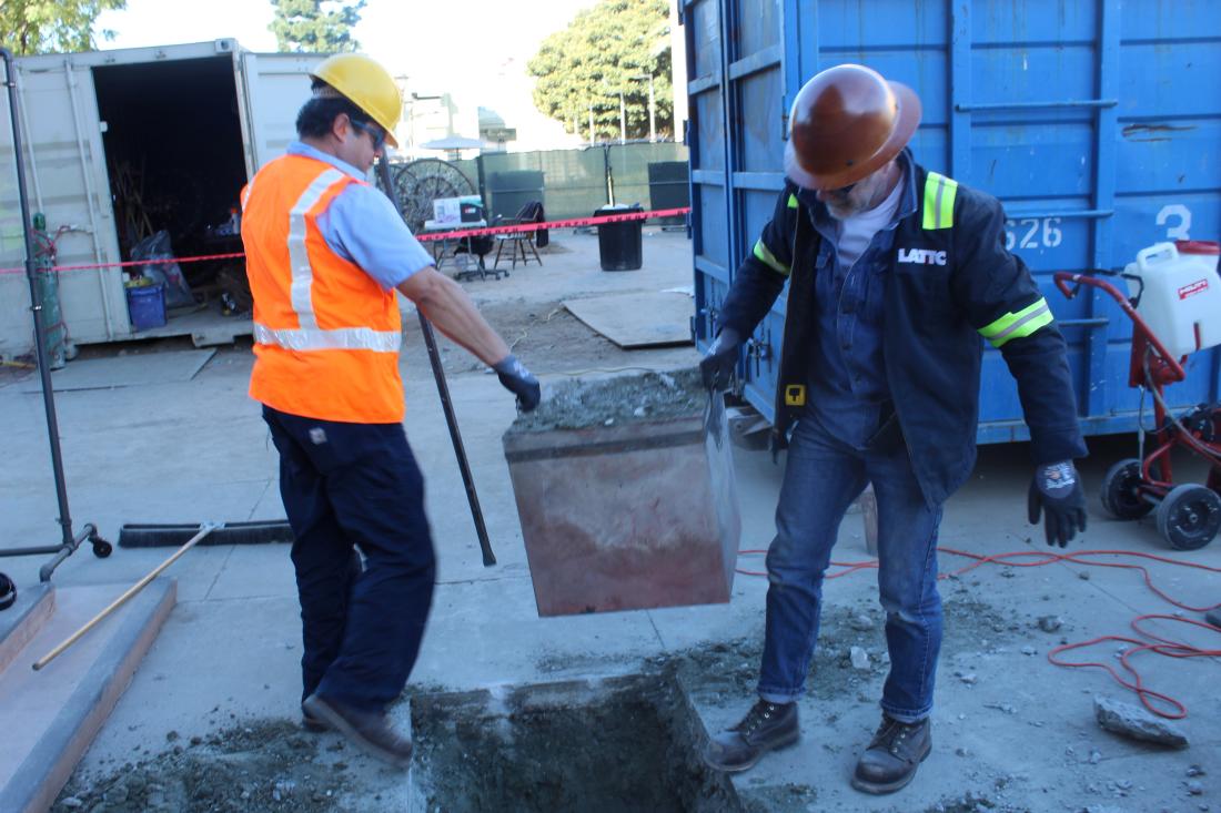 Physical plant workers lifting time capsule out of ground