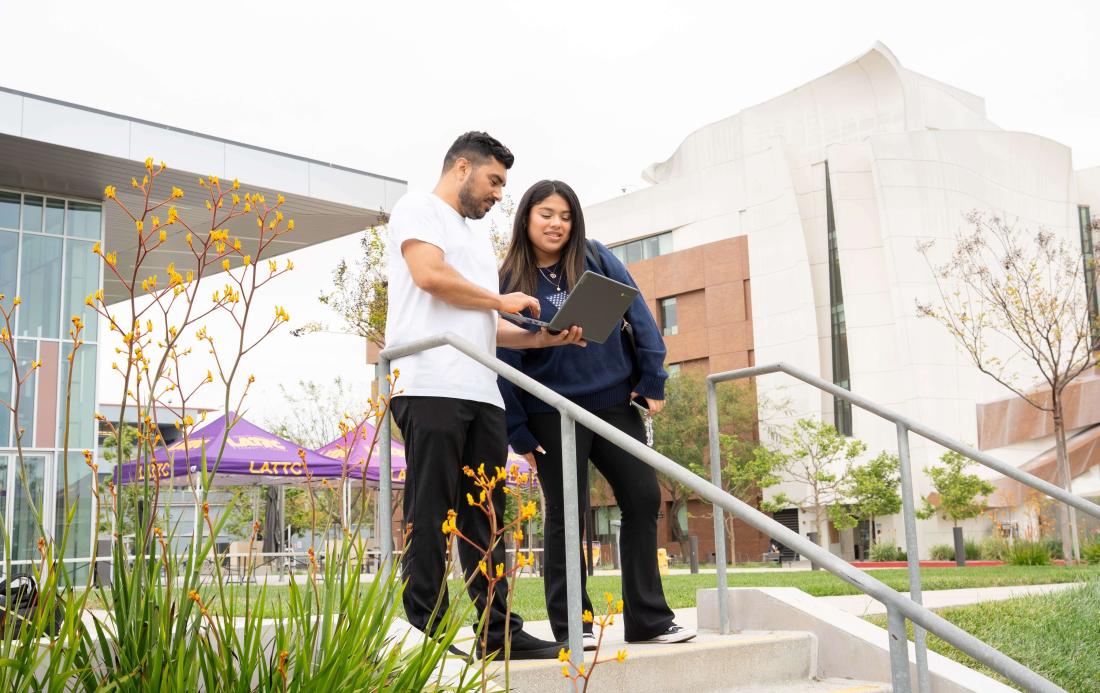 Students walking on campus while looking at a laptop