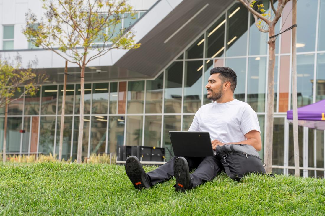 Student sitting on grass while working on laptop