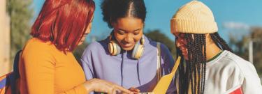 Three students looking at phone together and smiling
