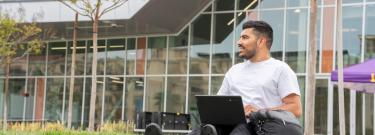 Student sitting on grass while working on laptop