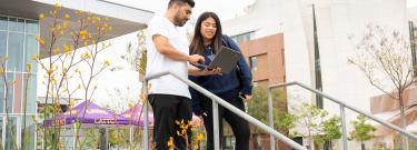 Students walking on campus while looking at a laptop