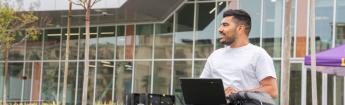 Student sitting on grass while working on laptop