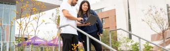 Students walking on campus while looking at a laptop